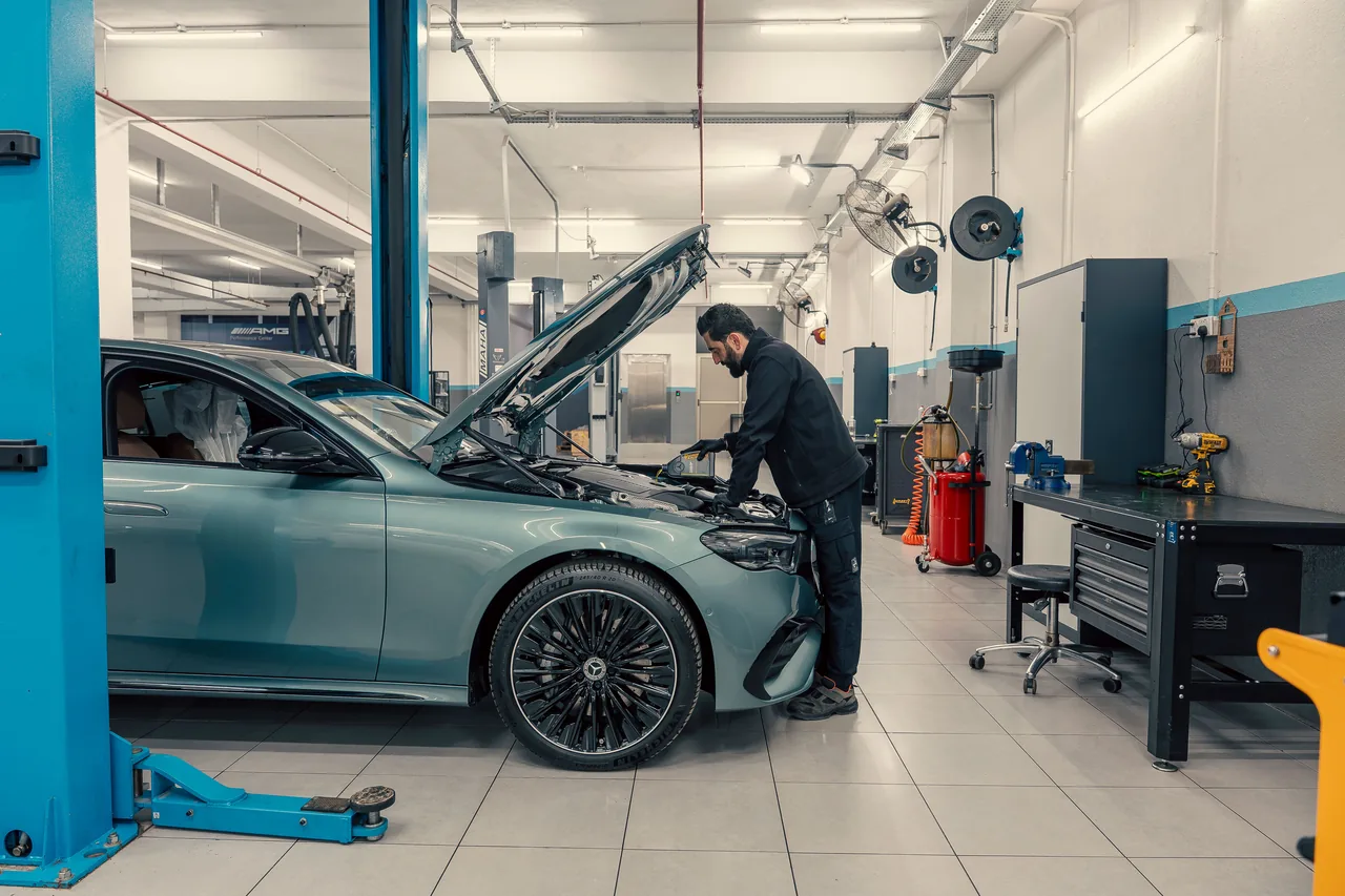 Techniker prüft den Motorraum eines Fahrzeugs in einer hellen Werkstatt